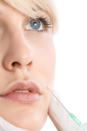 Woman with blue eyes looks upward as her doctor injects a dermal filler in her laugh lines